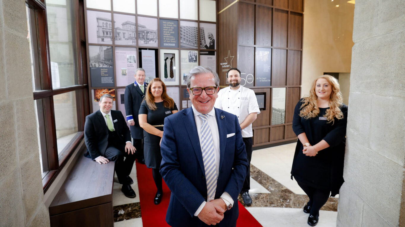 Welcoming hotel team in elegant lobby with historical displays, offering friendly service for a comfortable stay.