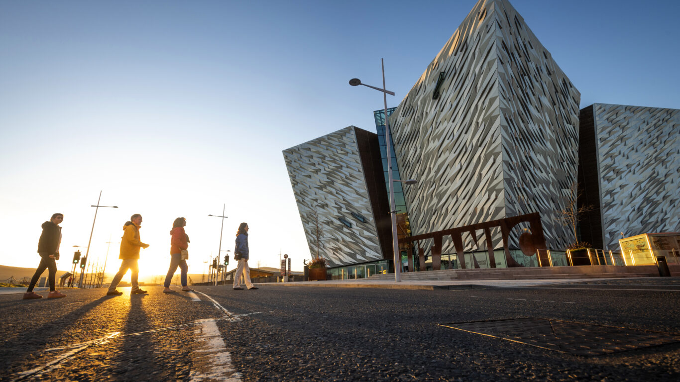 Guests enjoying a sunset walk by the iconic Titanic Belfast building featuring striking architecture and a warm ambience.