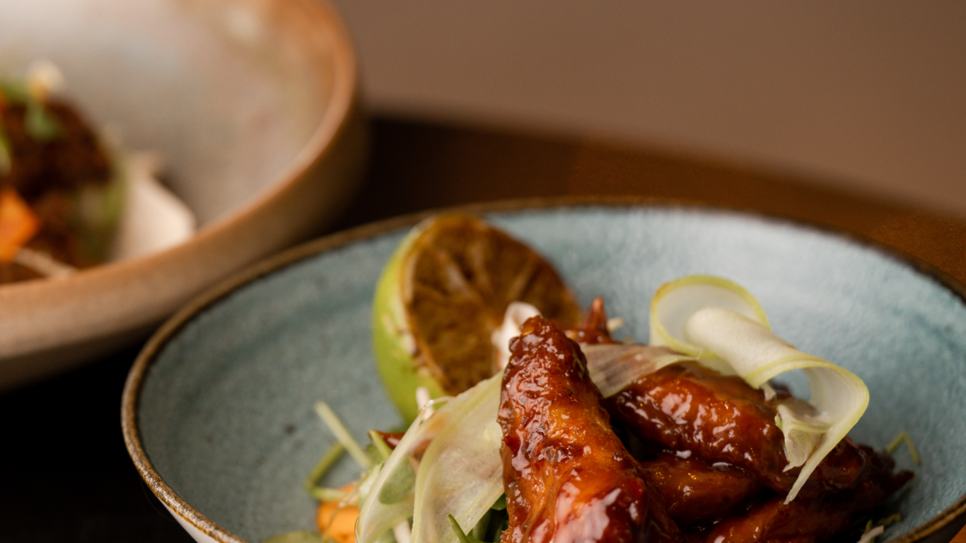 Savoury barbecue chicken wings with fresh garnish on rustic stoneware plate, offering a taste of hotel dining elegance.