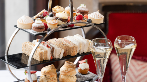 Elegant afternoon tea with tiered cakes, sandwiches, scones, and champagne in a cosy, luxurious hotel lounge setting.