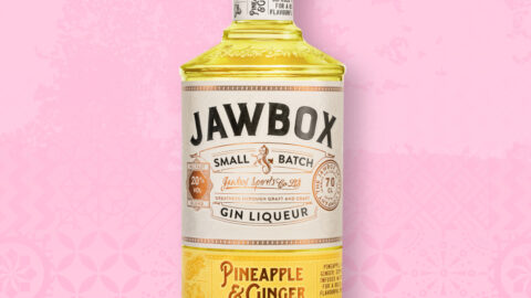 A bottle of yellow Jawbox Gin o a pink background