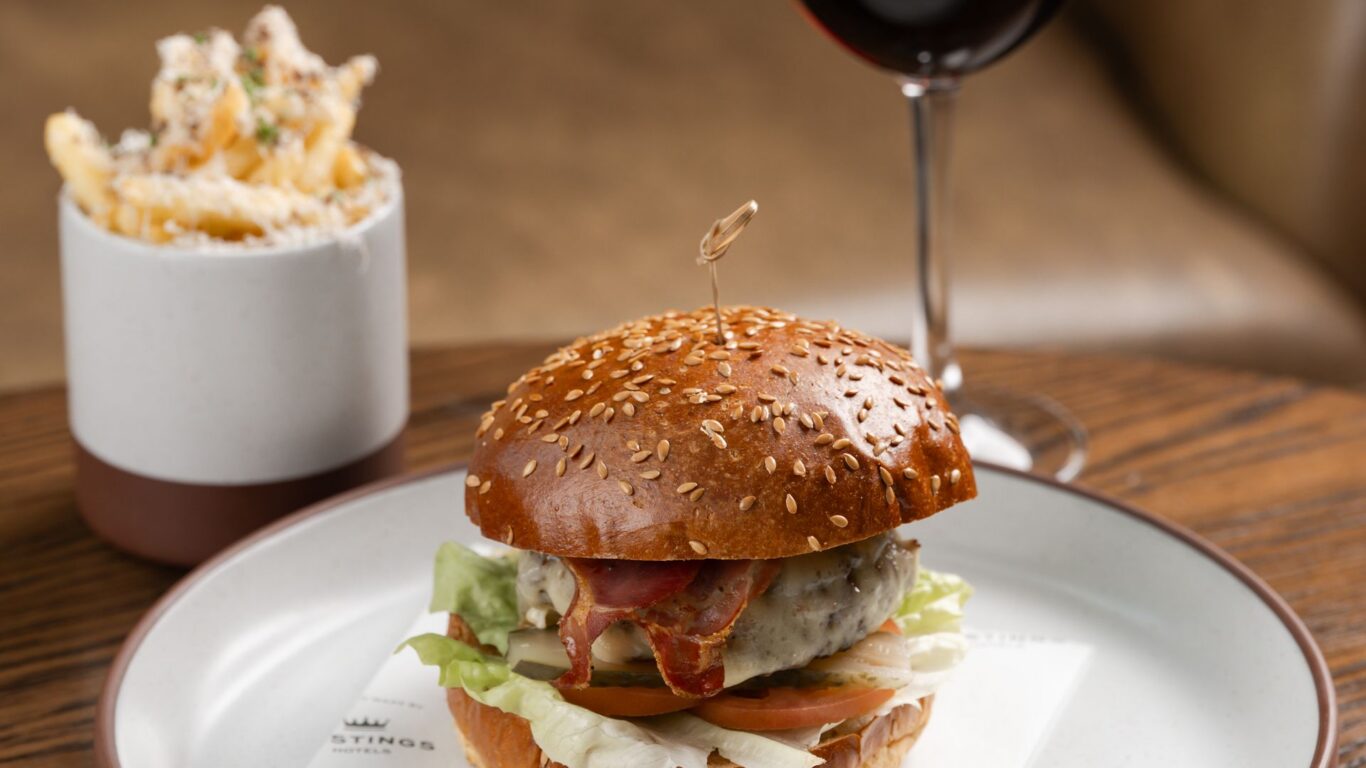 Gourmet bacon cheeseburger on sesame brioche with lettuce and tomato, truffle fries in a pot and a glass of red wine &mdash; cosy hotel dining.