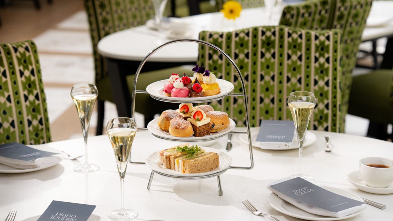 Elegant three-tier afternoon tea stand with finger sandwiches, scones and delicate pastries, served with champagne flutes in a bright hotel lounge